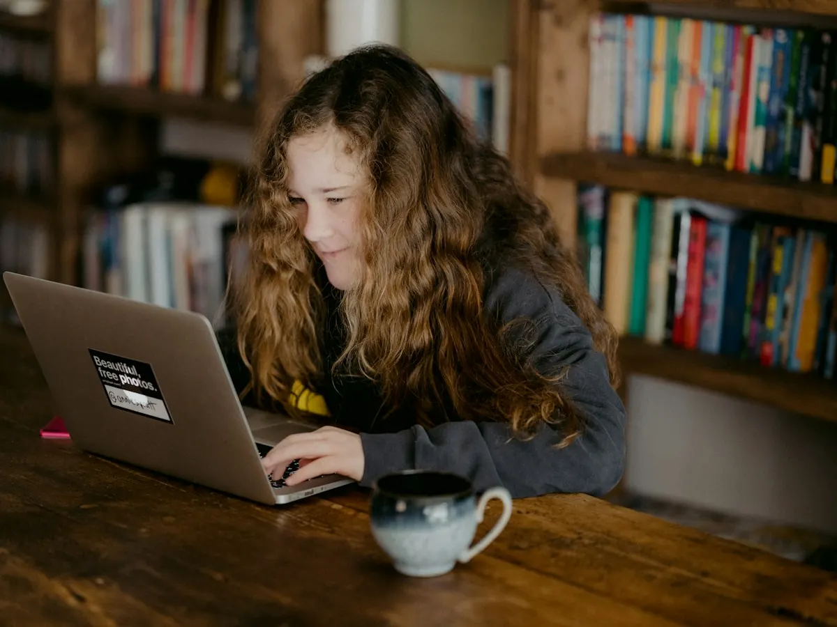 A teenage girl working on her laptop at a kitchen table