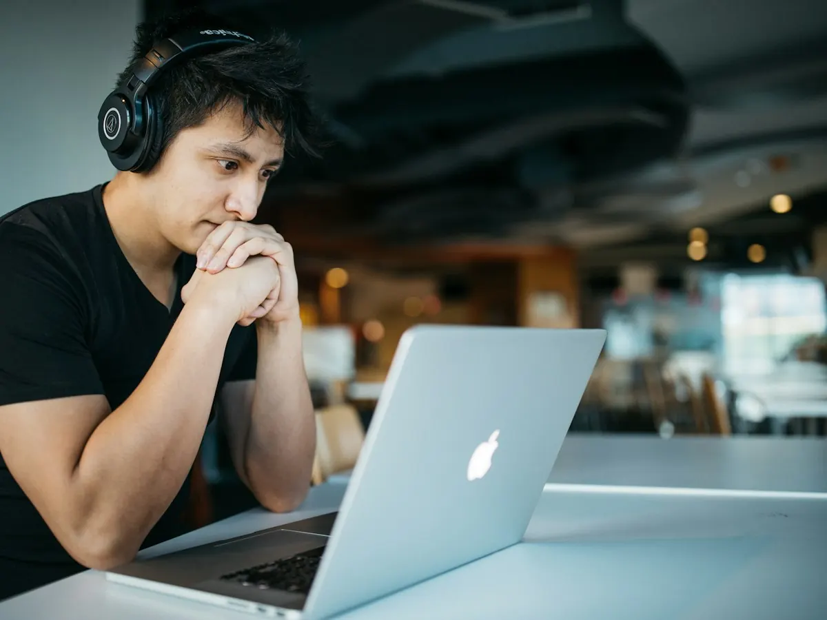 A student with headphones thinking through a problem at his laptop